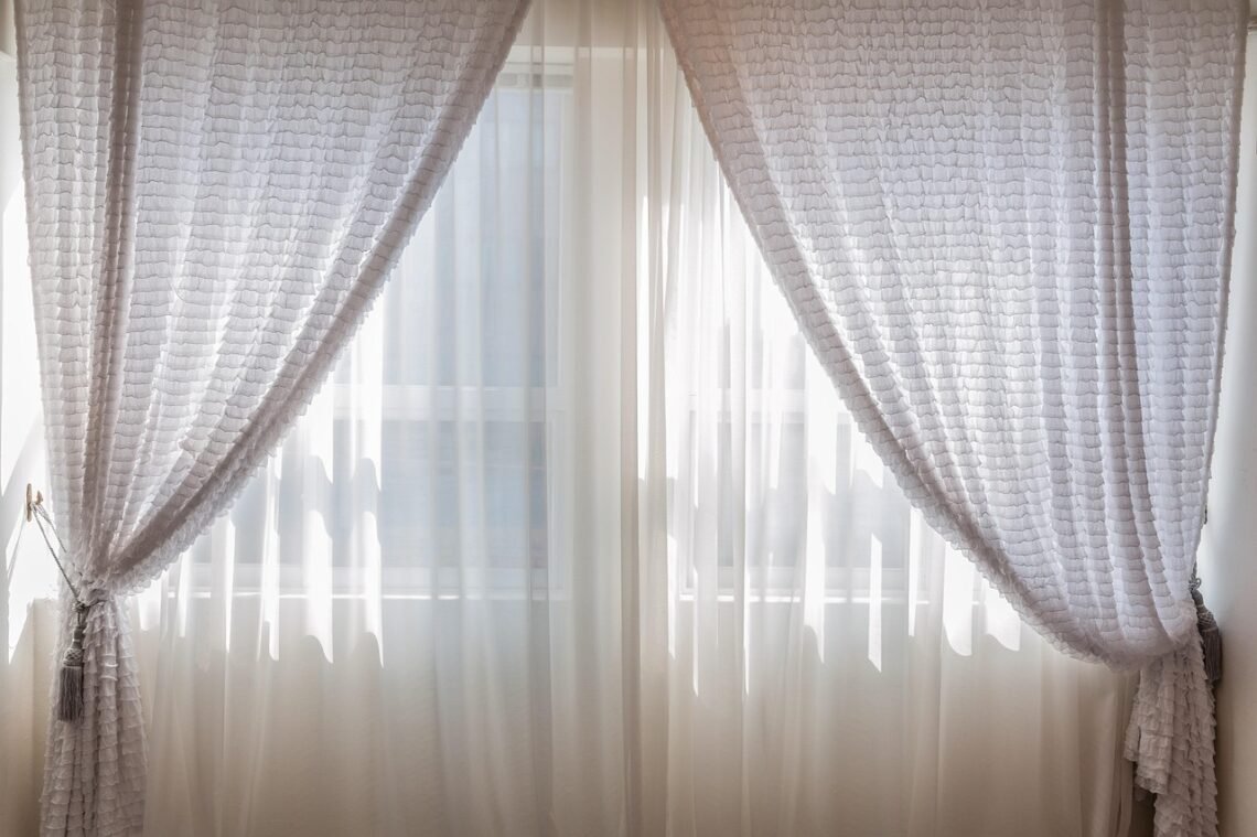 Soft natural light filters through sheer white curtains tied back with textured tassels, creating a serene, airy, and peaceful home atmosphere perfect for calm and cozy interior styling.