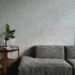 Minimalist living room corner with textured gray sofa and wooden side table, featuring a small potted plant and neutral decor, evoking calm, cozy, and inviting home ambiance.