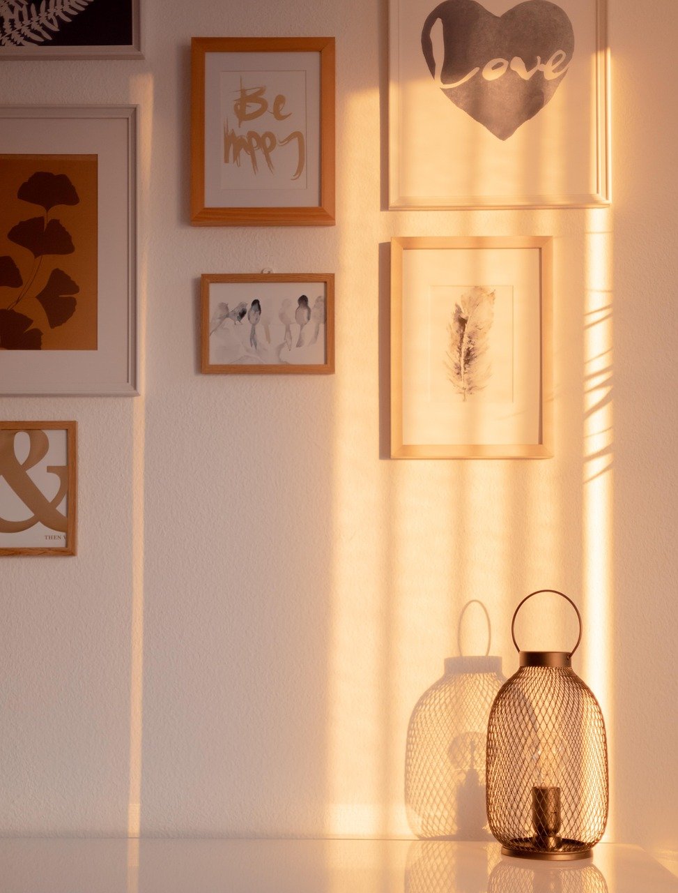 Sunlit wall with framed artwork and a decorative glass lantern, creating a warm, cozy, and inviting corner for a serene home atmosphere.