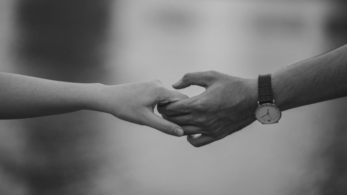 Two hands gently holding each other in black and white, symbolizing intimacy, connection, and cozy at-home date moments