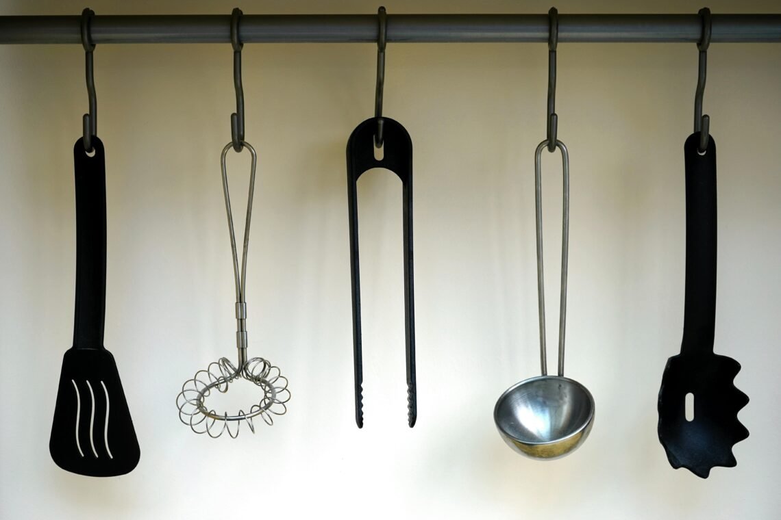 Minimalist kitchen utensils hanging on a metal rod, including a spatula, whisk, tongs, ladle, and pasta server, styled against a neutral wall for an organized, cozy, and functional kitchen aesthetic.