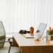 Minimalist home office setup with a wooden desk, laptop, white coffee mug, potted cactus, camera, and organized stationery, evoking calm, focused work-from-home environment.