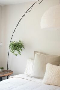 Cozy bedroom corner with soft neutral bedding, a tall arc floor lamp, and a small potted plant on a wooden nightstand creating a serene and relaxing atmosphere for a calm home.