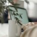 Close-up of a white coffee mug on a desk in a calm, cozy workspace, with blurred laptop and greenery in the background, evoking focus and relaxed productivity.