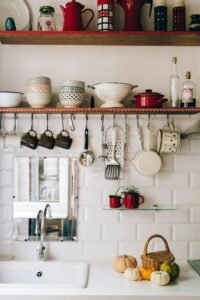 Organized kitchen shelves with white dishes, hanging utensils, and jars on a white subway tile backsplash for a clean and cozy home aesthetic.