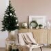 A minimalistic winter living room scene featuring a small decorated Christmas tree, neutral-toned wrapped gifts, a beige throw draped over a wooden chair, and a wooden sideboard adorned with a wreath, candles, and small greenery for a cozy, seasonal aesthetic.