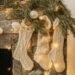 Three cream-colored knit Christmas stockings hanging from a stone fireplace mantel, adorned with greenery and warm string lights, creating a cozy and festive winter ambiance.
