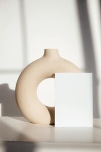 Minimalist beige ceramic vase and white block decor on a sunlit surface, creating a clean and serene accent for cozy home styling.