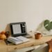 Minimalist fall workspace with a wooden desk, laptop, planner, warm coffee mug, small pumpkins, and a leafy green plant, styled with neutral and cozy seasonal accents.