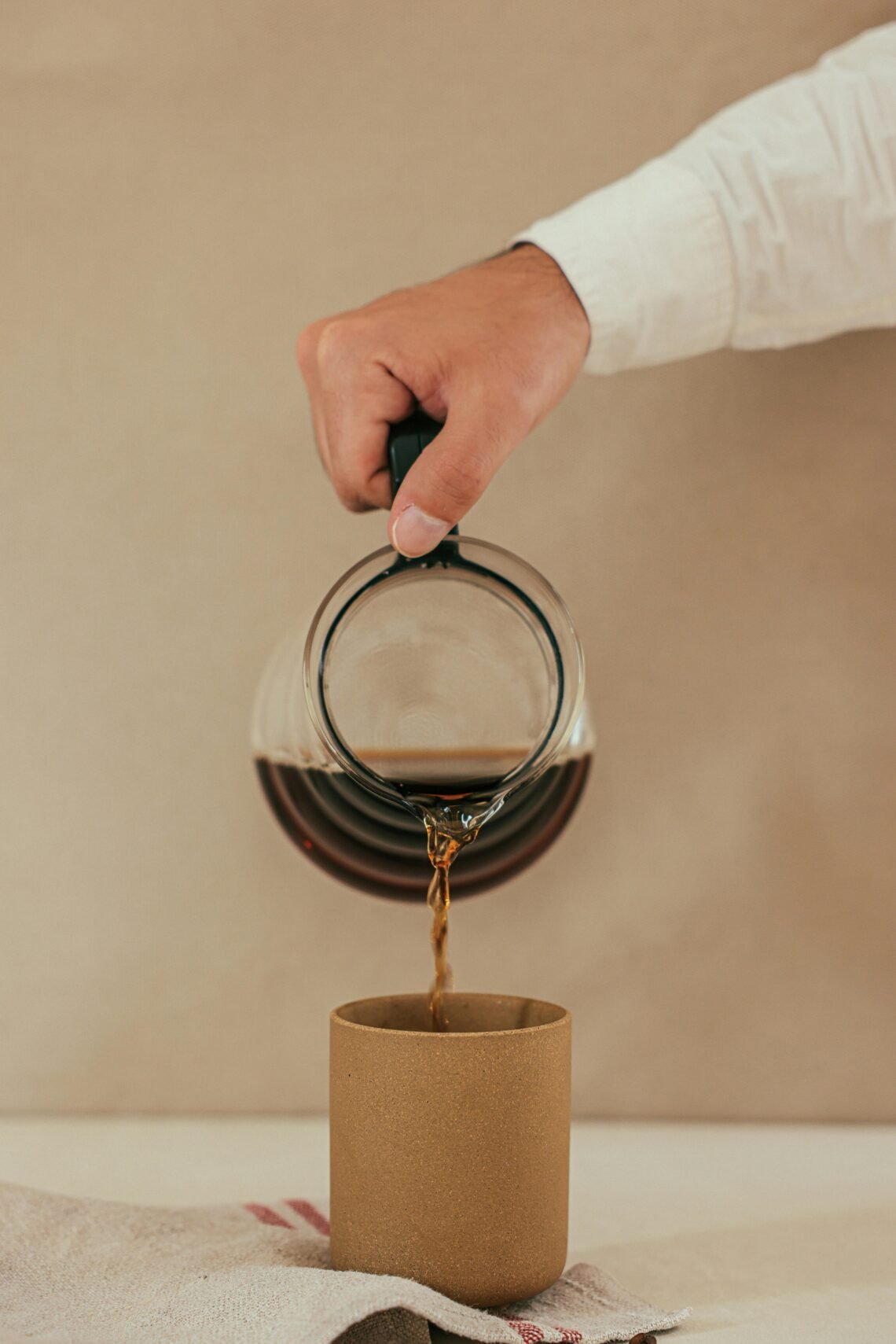 Pouring freshly brewed coffee into a neutral mug, creating a cozy and luxurious morning coffee ritual for self-care and mindful daily wellness.