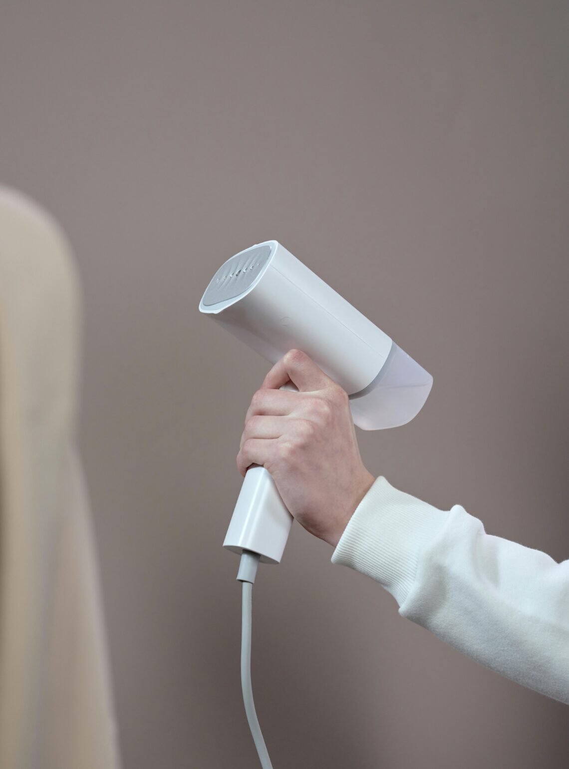 Hand holding a white hair dryer against a minimalist gray background in a studio setting.