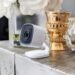 Modern white indoor security camera styled on a neutral home console table beside gold accents and soft florals, showing how useful home upgrades can add safety and style to your space.