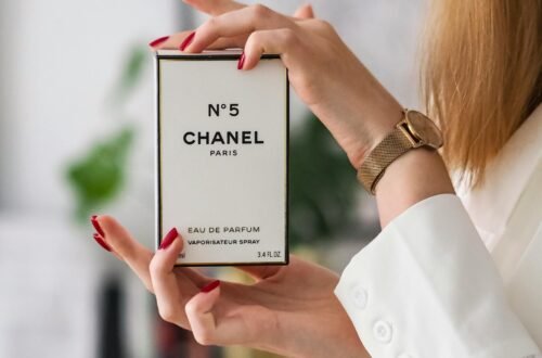Woman holding a Chanel No. 5 perfume box in a soft, elegant setting, showcasing a luxury fragrance for women available on Amazon. Clean neutral background with feminine details