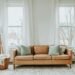 Warm neutral living room with a tan leather sofa, soft white curtains, and minimal cozy decor — a calm, inviting example of simple cozy living room upgrades that transform a space into a peaceful retreat.