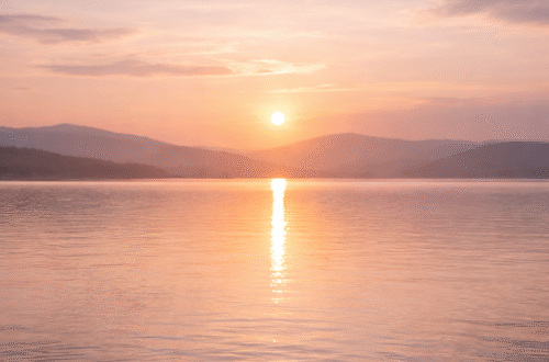 soft pastel sunrise over calm lake water with gentle ripples and muted clouds creating a peaceful minimalist scene that evokes quiet mornings slow living and intentional calm