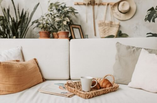 Cozy living room accent pieces styled on a white sofa with neutral pillows, a woven tray, coffee mug, greenery, and warm natural decor for a soft, inviting home look